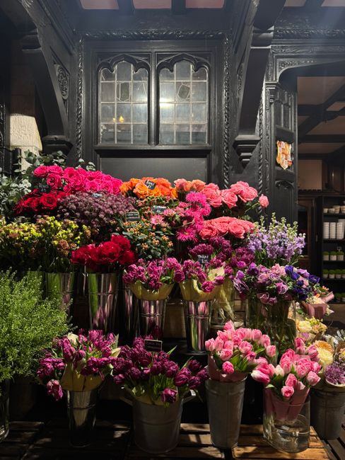 An indoor display of numerous floral arrangements featuring a variety of fresh flowers, including pink, red, purple, and orange blooms such as carnations and chrysanthemums, arranged in tall, sleek me